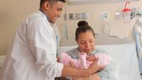 Male resident hands newborn baby to mother.